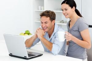 Happy Couple Looking At Something On The Laptop While Drinking Coffee